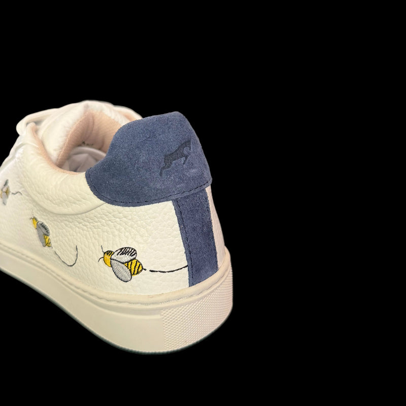 White sneaker with blue accents and bee designs on a dark surface